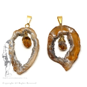 Agate geode slice pendants with citrine crystals linked in the middle featuring gold plated bails against a white background