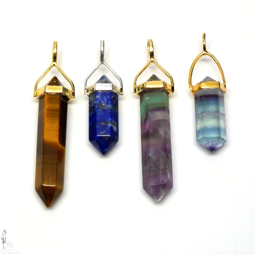 4 simple crystal-shaped pendants made from vogel cut tiger's eye, lapis lazuli, and fluorite set in sterling silver or gold plated against a white background.