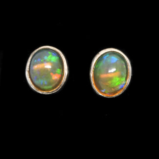 A pair of colorful ethiopian opal cabochons set into simple sterling silver stud earrings against a black background