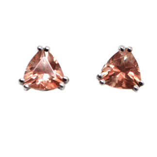 A pair of peach toned oregon sunstone gemstones cut and faceted into a trilliant and set into sterling silver stud earrings against a white background