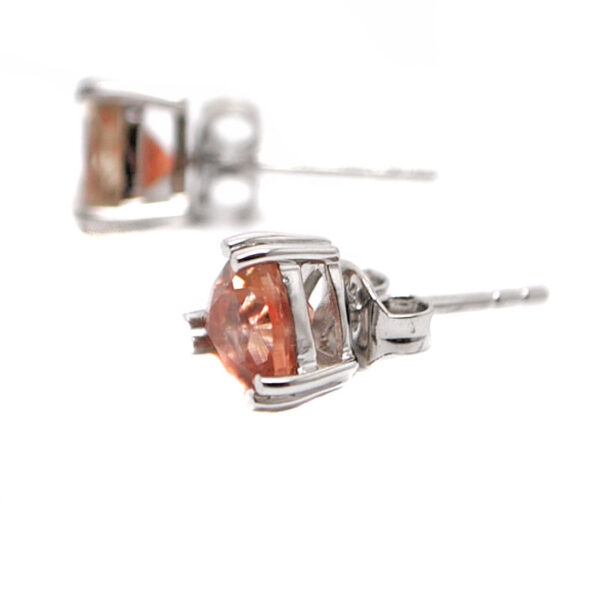 A pair of peach toned oregon sunstone gemstones cut and faceted into a trilliant and set into sterling silver stud earrings against a white background