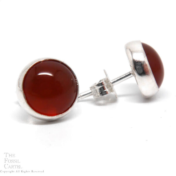 A pair of dark orange carnelian agate circular cabochons set in in sterling silver earring studs against a white background