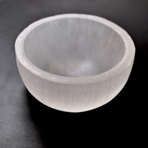 A piece of selenite carved into a small bowl against a black background