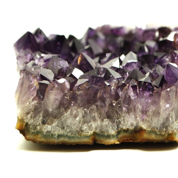 A side view of a purple amethyst crystal cluster with agate banding along the edges of the cluster against a white background