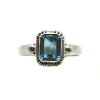 A blue topaz gemstone faceted into a rectangle shape and set in a decorative sterling silver ring against a white background