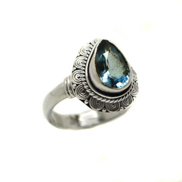 A blue topaz gemstone faceted into a teardrop shape and set in an intricate sterling silver ring against a white background