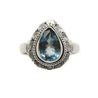 A blue topaz gemstone faceted into a teardrop shape and set in an intricate sterling silver ring against a white background