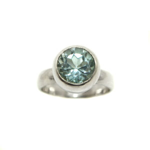 A round blue topaz faceted gemstone set into a sterling silver ring against a white background