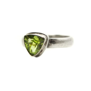 A peridot gemstone faceted into a trilliant and set into a simple sterling silver ring with a thin band against a white background