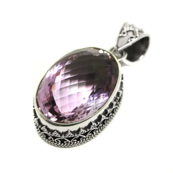 An amethyst faceted and set into an intricate sterling silver pendant against a white background