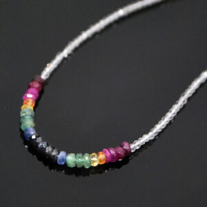 A topaz and rainbow corundum microbead necklace against a black background