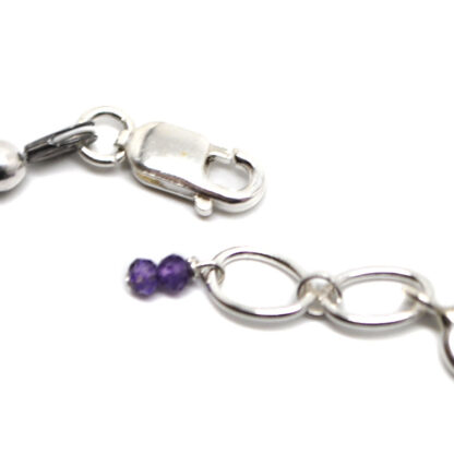 A deep purple amethyst microbead bracelet with a sterling silver lobster claw clasp against a black background