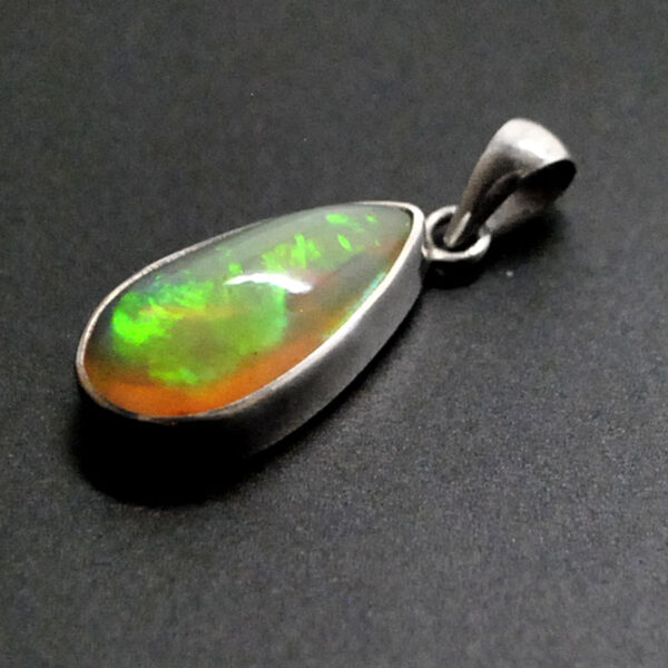 A sterling silver teardrop pendant featuring an ethiopian opal with green and red play of color against a black background