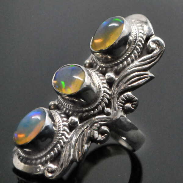 An ornate sterling silver ring featuring 3 oval ethiopian opals with rainbow play of color against a black background