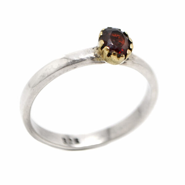 A sterling silver ring with a faceted deep red garnet gemstone set into a brass bezel against a white background