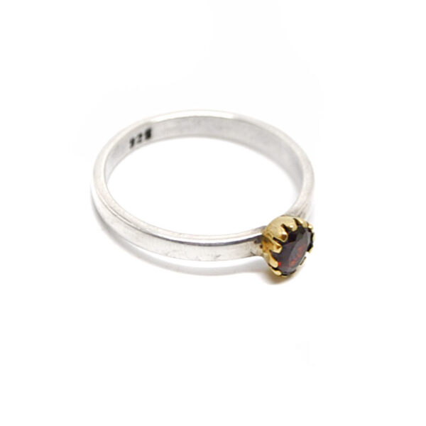 A sterling silver ring with a faceted deep red garnet gemstone set into a brass bezel against a white background