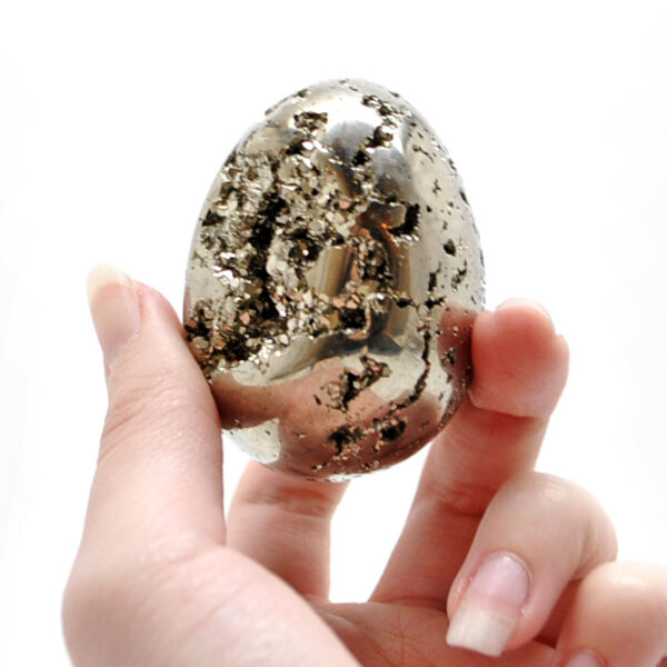 A hand holding a carved pyrite egg with exposed crystals against a white background