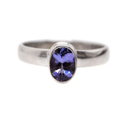 An oval faceted tanzanite gemstone set into a simple sterling silver ring against a white background
