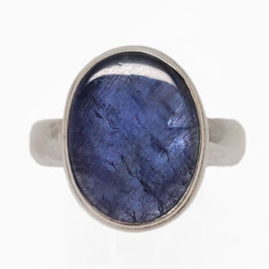 An oval tazanite cabochon set into a simple sterling silver ring against a white background