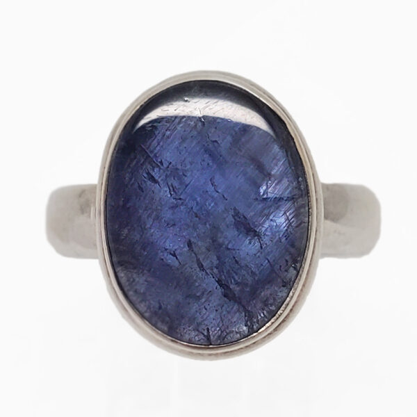 An oval tazanite cabochon set into a simple sterling silver ring against a white background