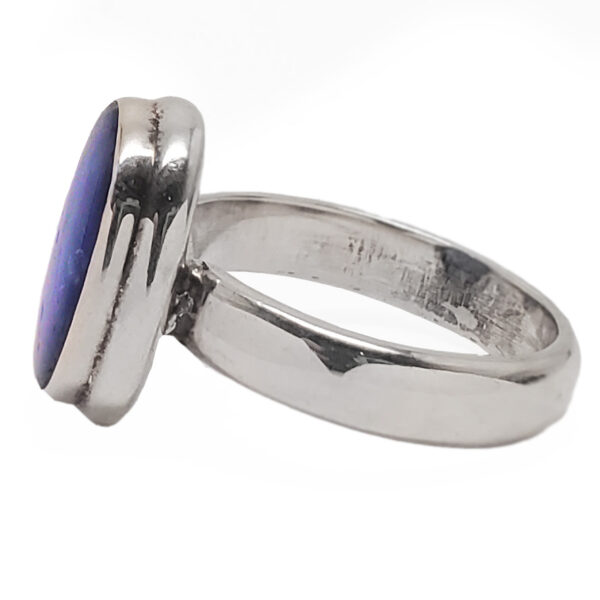 An oval tazanite cabochon set into a simple sterling silver ring from the side against a white background