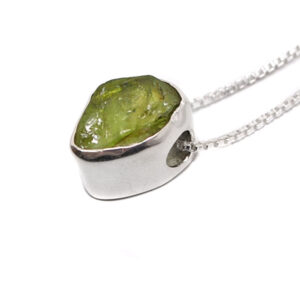 A sterling silver pendant set with a rough peridot gemstone with a box chain necklace against a white background