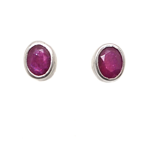 A pair of sterling silver stud earrings set with oval faceted ruby gemstones against a white background