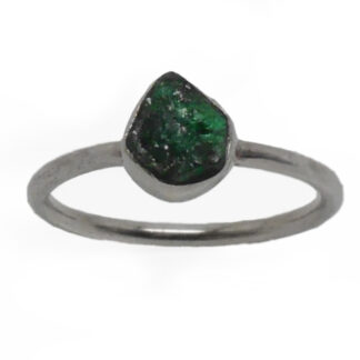 A rough emerald set into a simple sterling silver ring against a white background