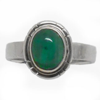 An carbochon emerald set into a simple sterling silver ring against a white background