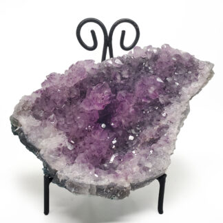 A large amethyst cluster on a black display stand against a white backround