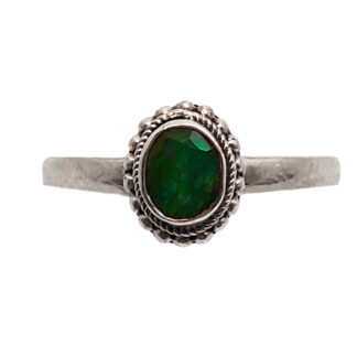 An oval faceted emerald set into a simple sterling silver ring against a white background