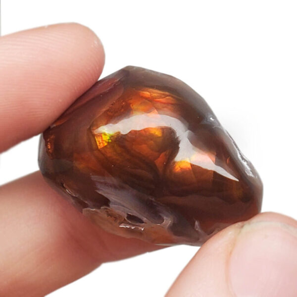 A fire agate shined and polished on one side held up by hand against a white background