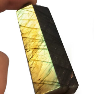 Labradorite Tower held by hand to display the angle with the brightest flash photographed against a white background