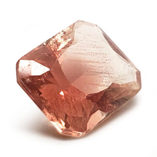 A faceted sunstone cut into a reatagular shape photographed behind a white background